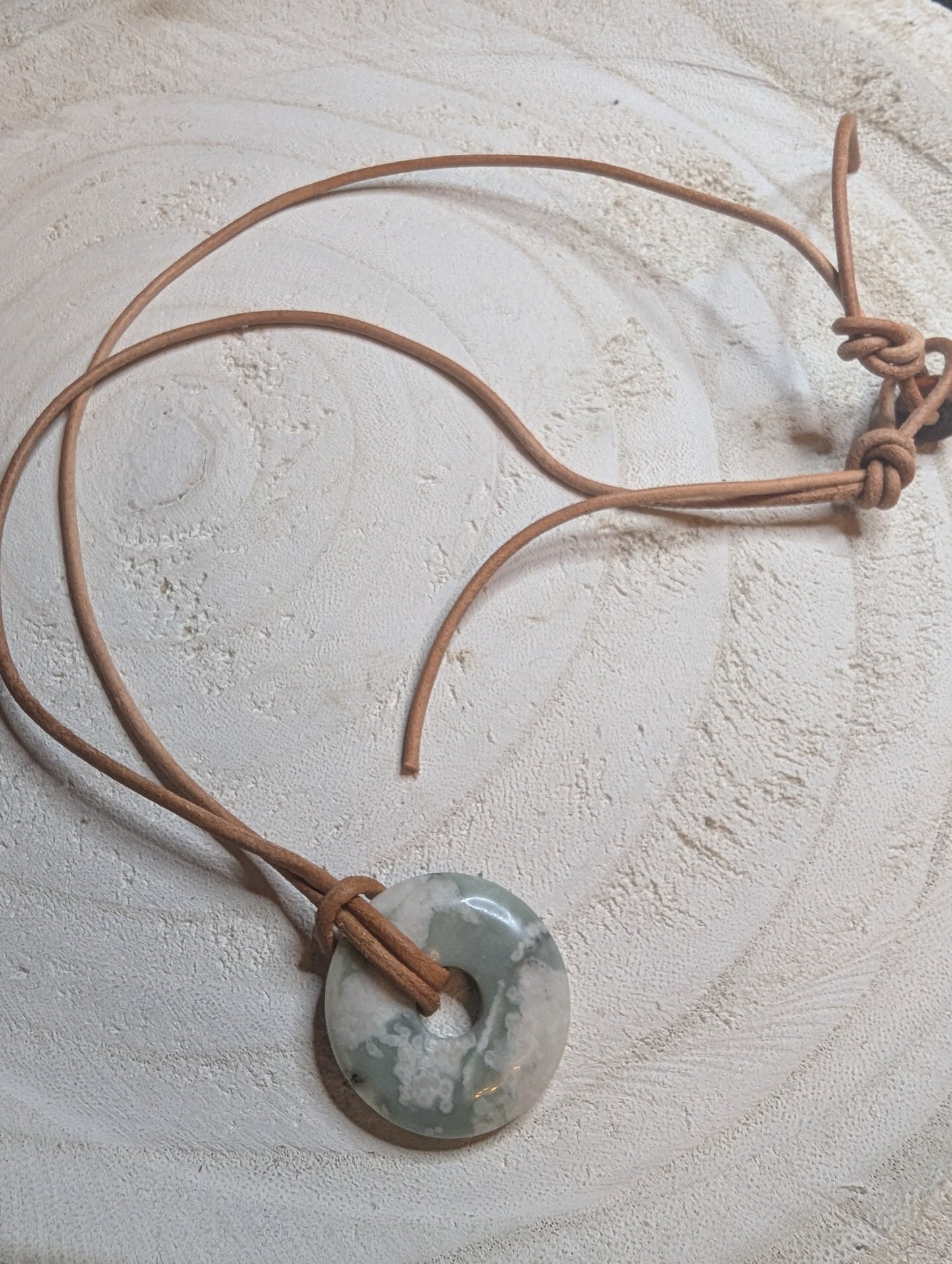 Necklace with a circular pendant with a beige leather cord