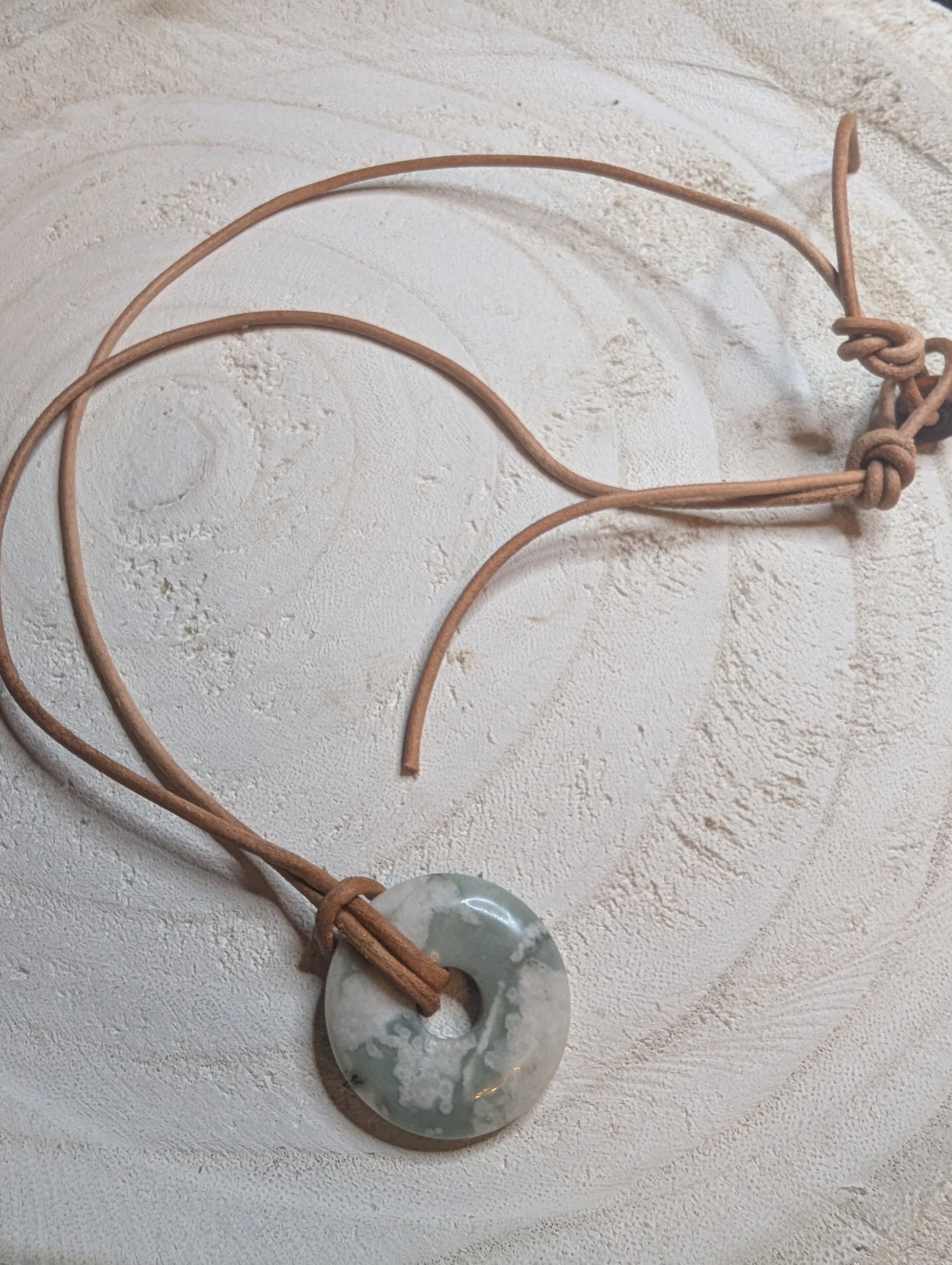 Necklace with a circular pendant with a beige leather cord
