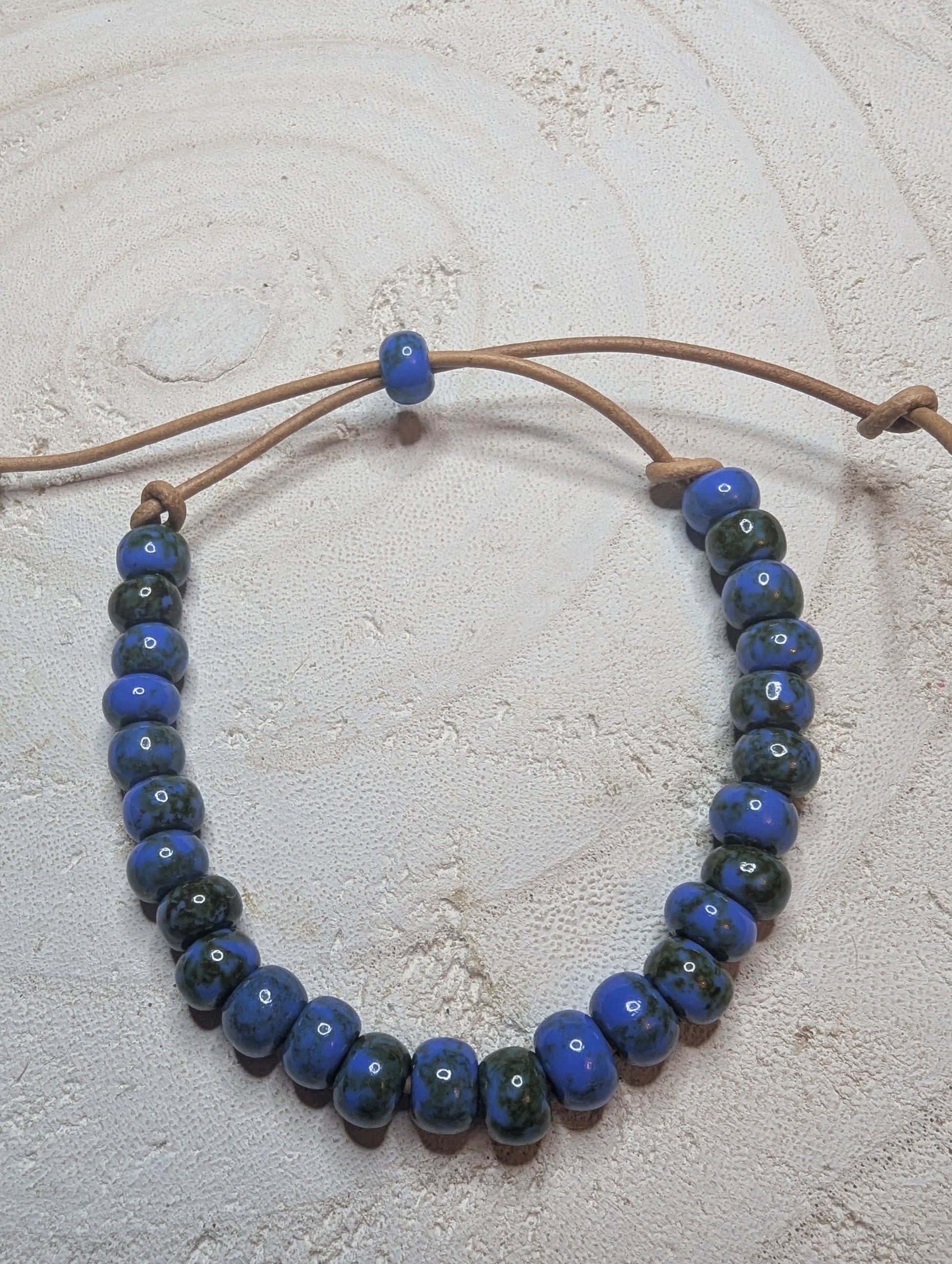 Adjustable beaded bracelet with blue and black beads on a beige cord 